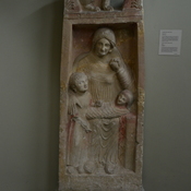 Idalion, Funerary stele of a young mother, holding a fruit in her left hand, with child and baby, crowned with a sphinx between two acroteria